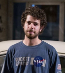 Young man with dark curly hair, beard and mustache and NASA T-shirt