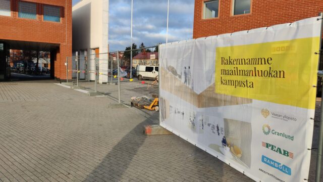 Luotsi's construction site from the inner yard side. In the front is a fence with an advertisement: Building a world-class campus.