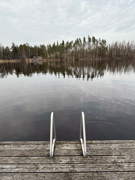 End of a jetty with the ladder leading to the water of the archipelago. Trees on an island in the background.