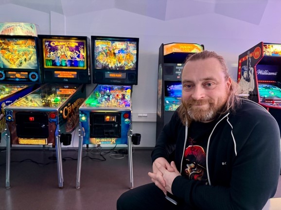 Teemu Närvä sitting in front of pinball machines at the University of Vaasa Games Centre
